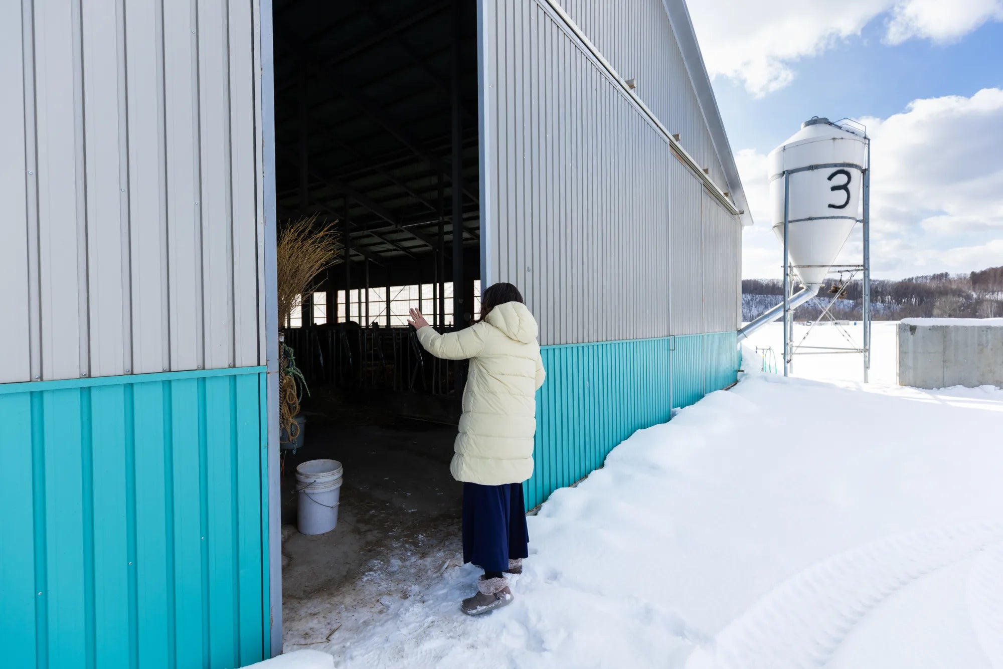 Ellie, a middle aged Japanese woman, waving goodbye to her cows in the barn as she closes the door for the day