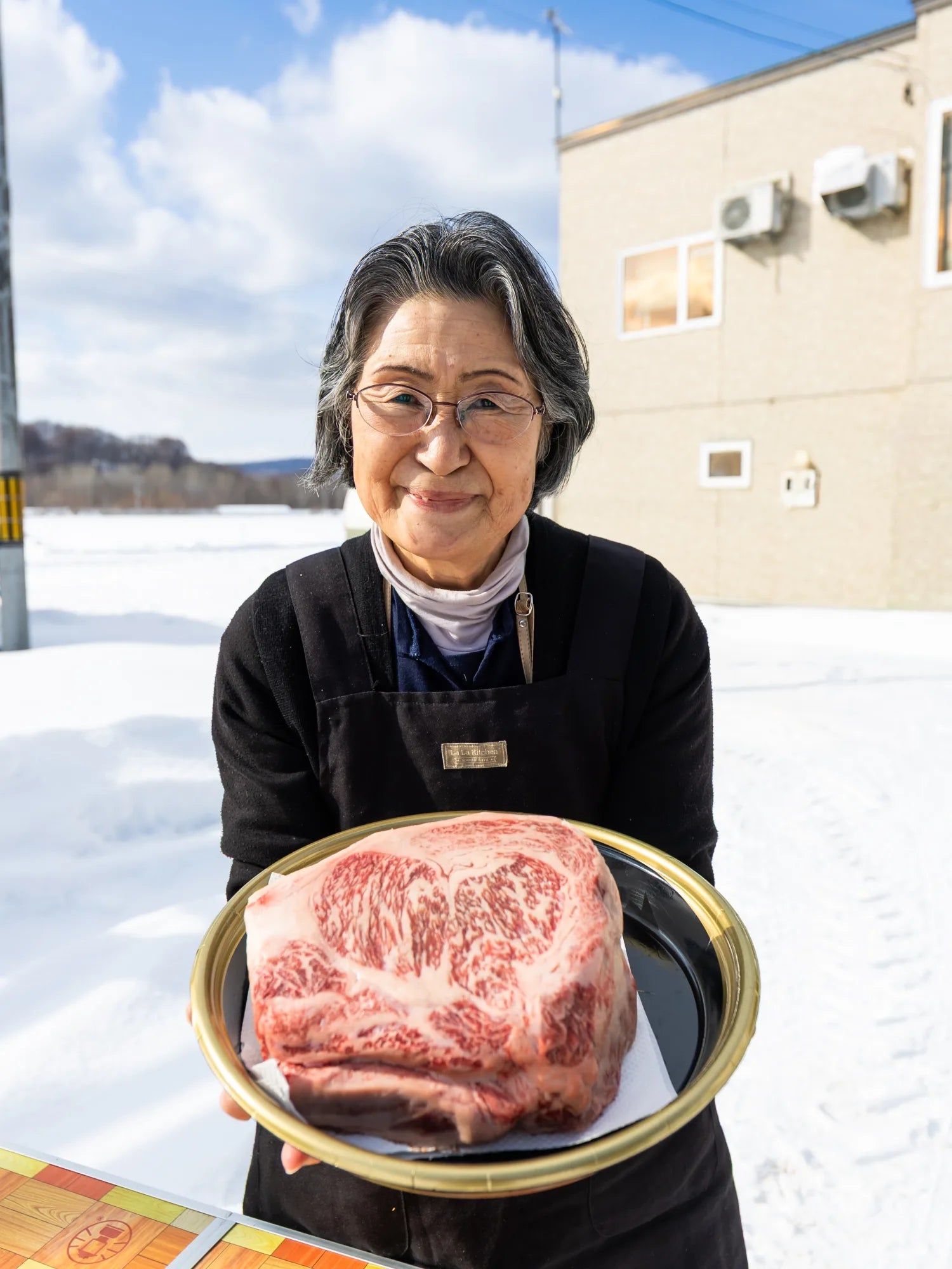 Tomoko-san, a friendly older Japanese woman, presenting the viewer with a beautiful ribeye